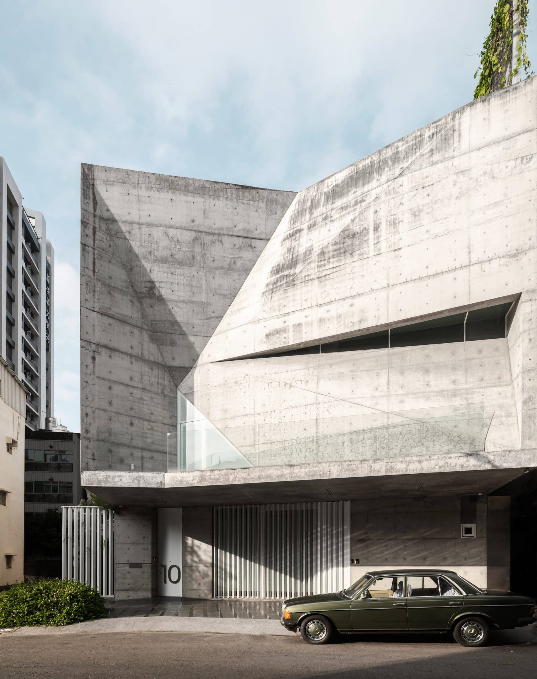Angular concrete exterior walls of a home with a black car parked in front