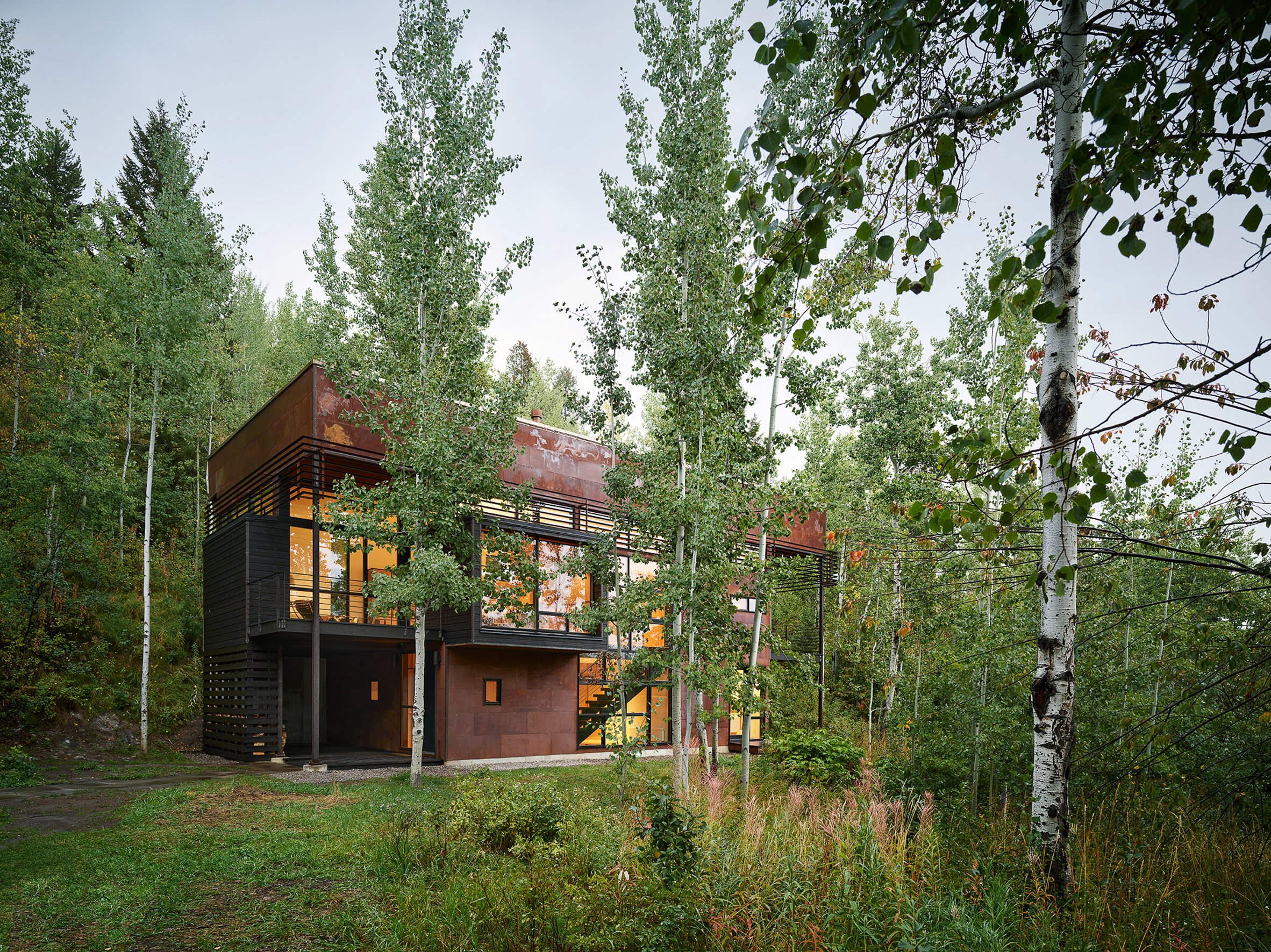 Rectilinear oxidised steel house surrounded by trees