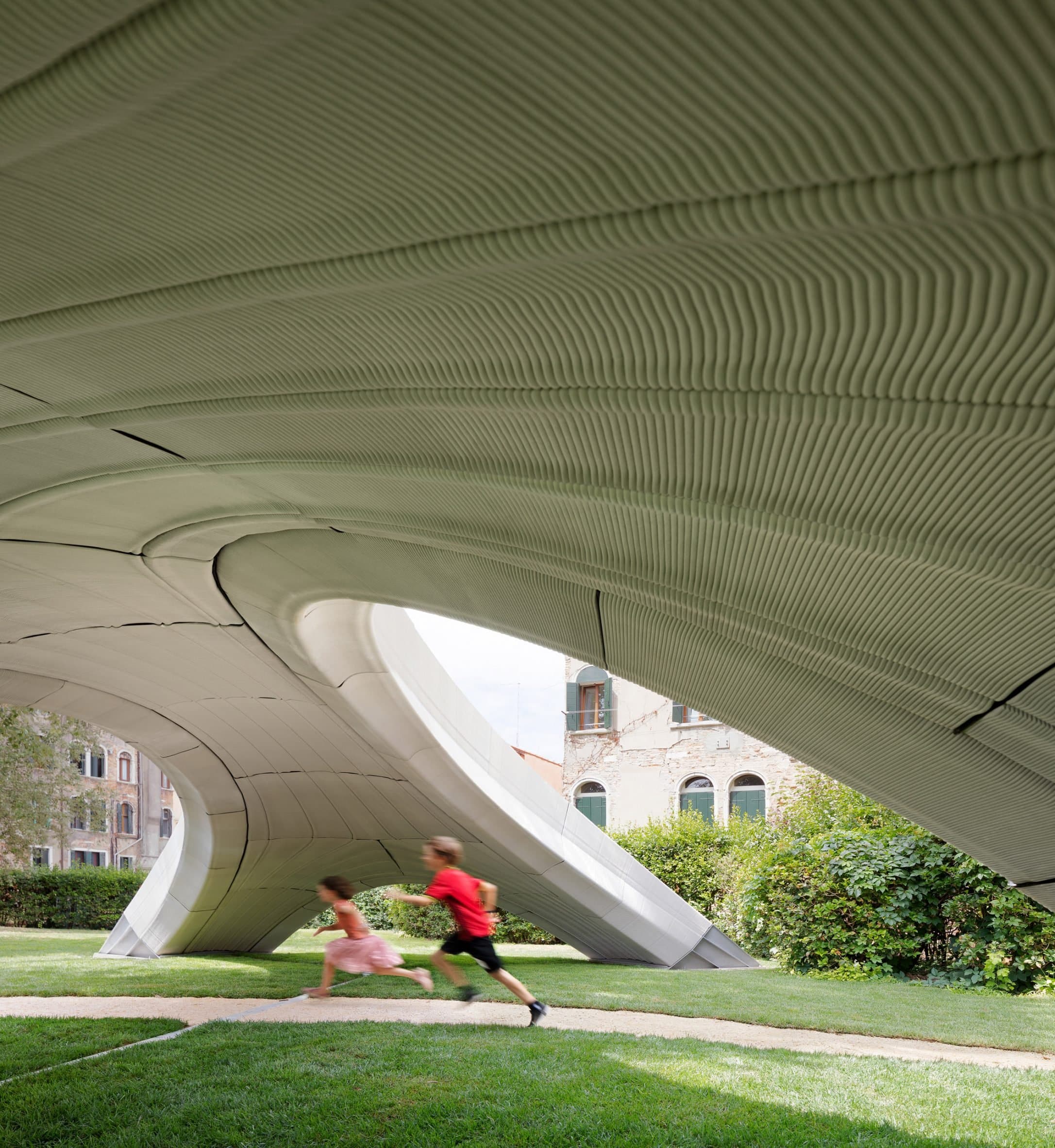 Two children running through the arches of the Striatus 3D-printed concrete footbridge