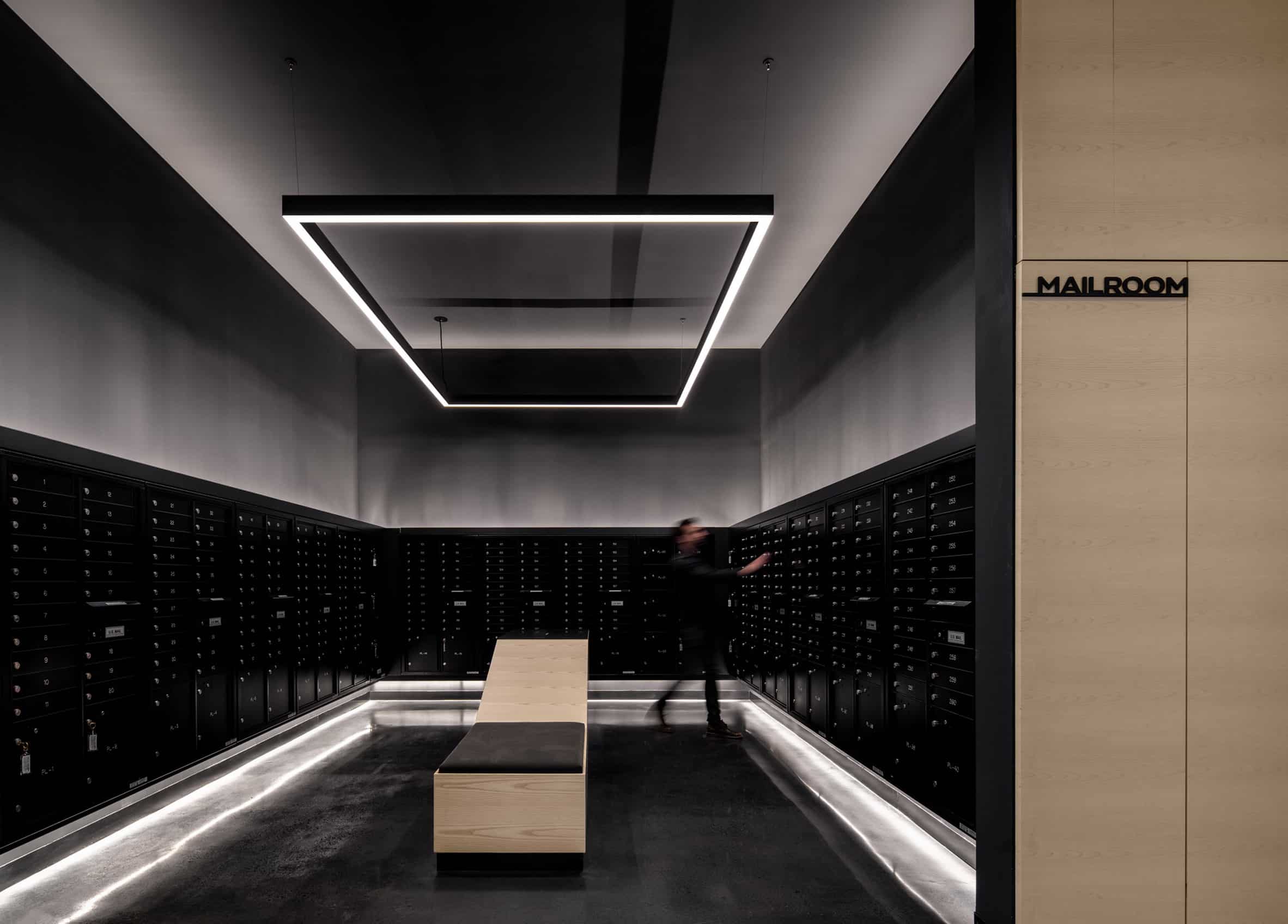 Black and silver mailroom within mixed-use building by Handel Architects with rectilinear LED lighting overhead