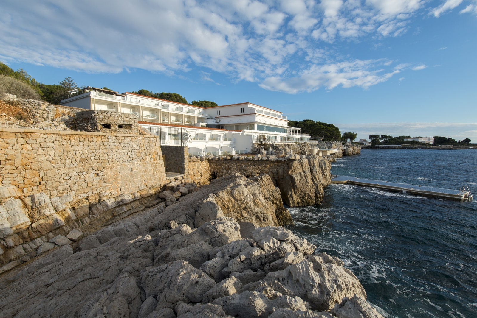 a white hotel built into a cliff on the side of the ocean