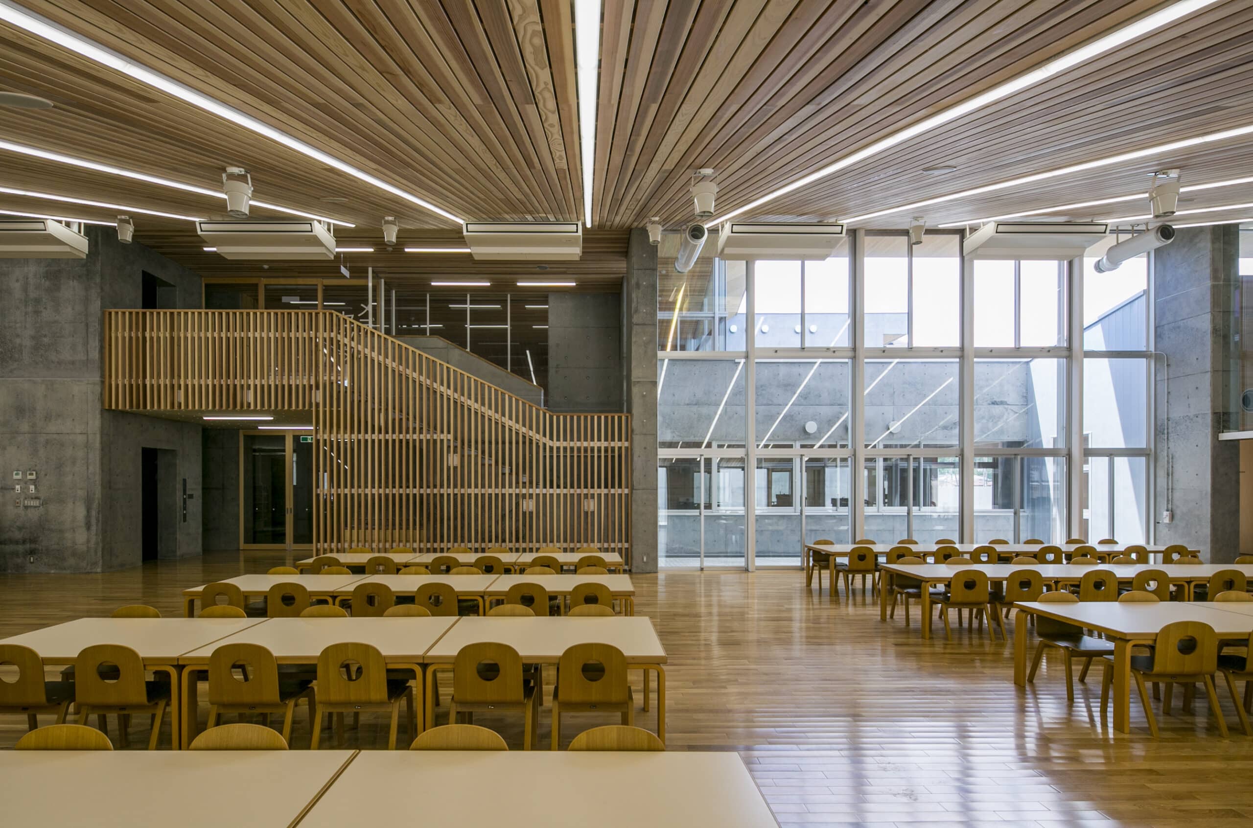 A two-storey common area of the school, seamlessly blending the natural warmth of wooden ceilings and floors with the sleek and modern aesthetic of concrete walls. 