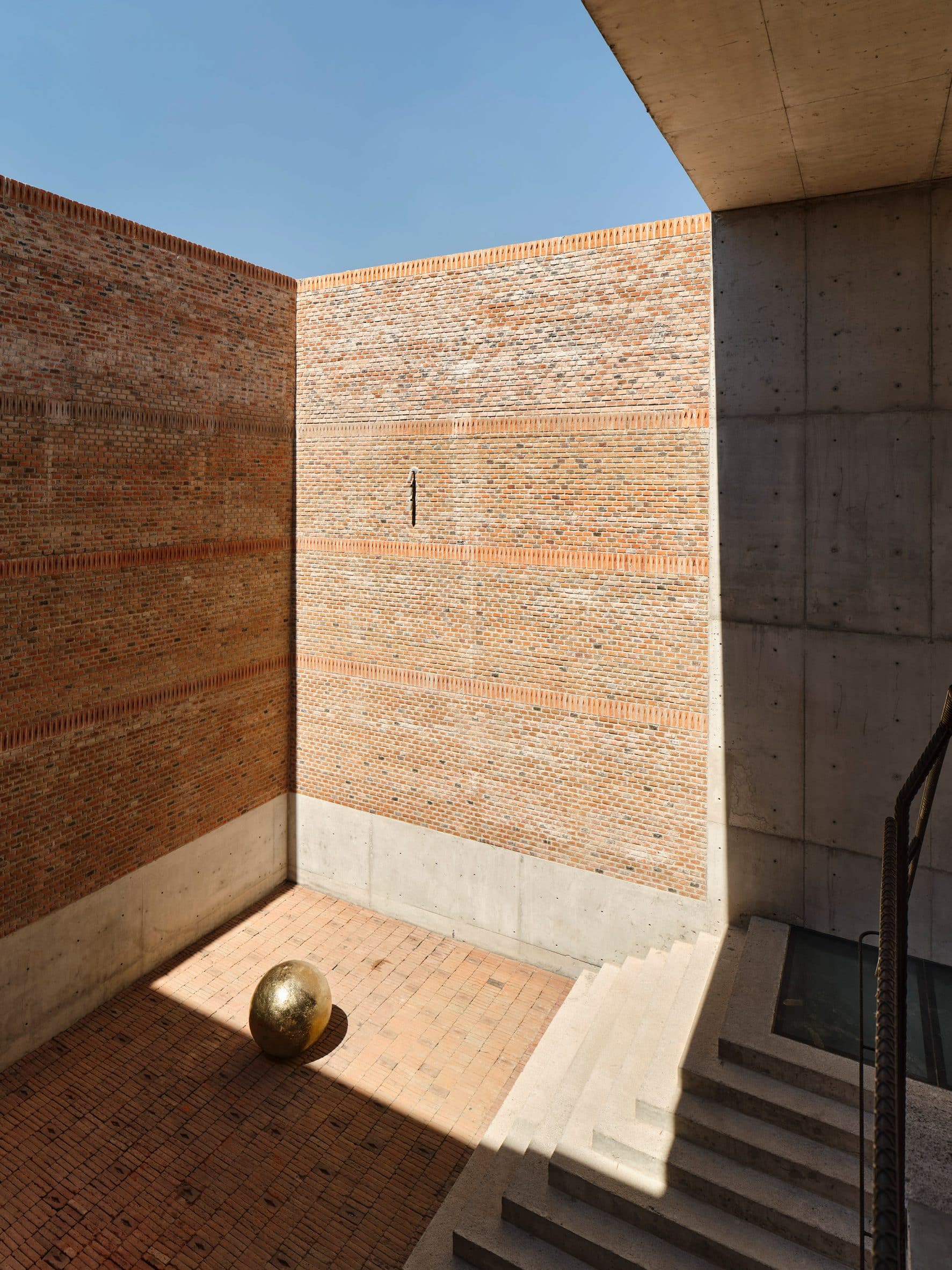 Open air space lined by brick with metal orb in the middle