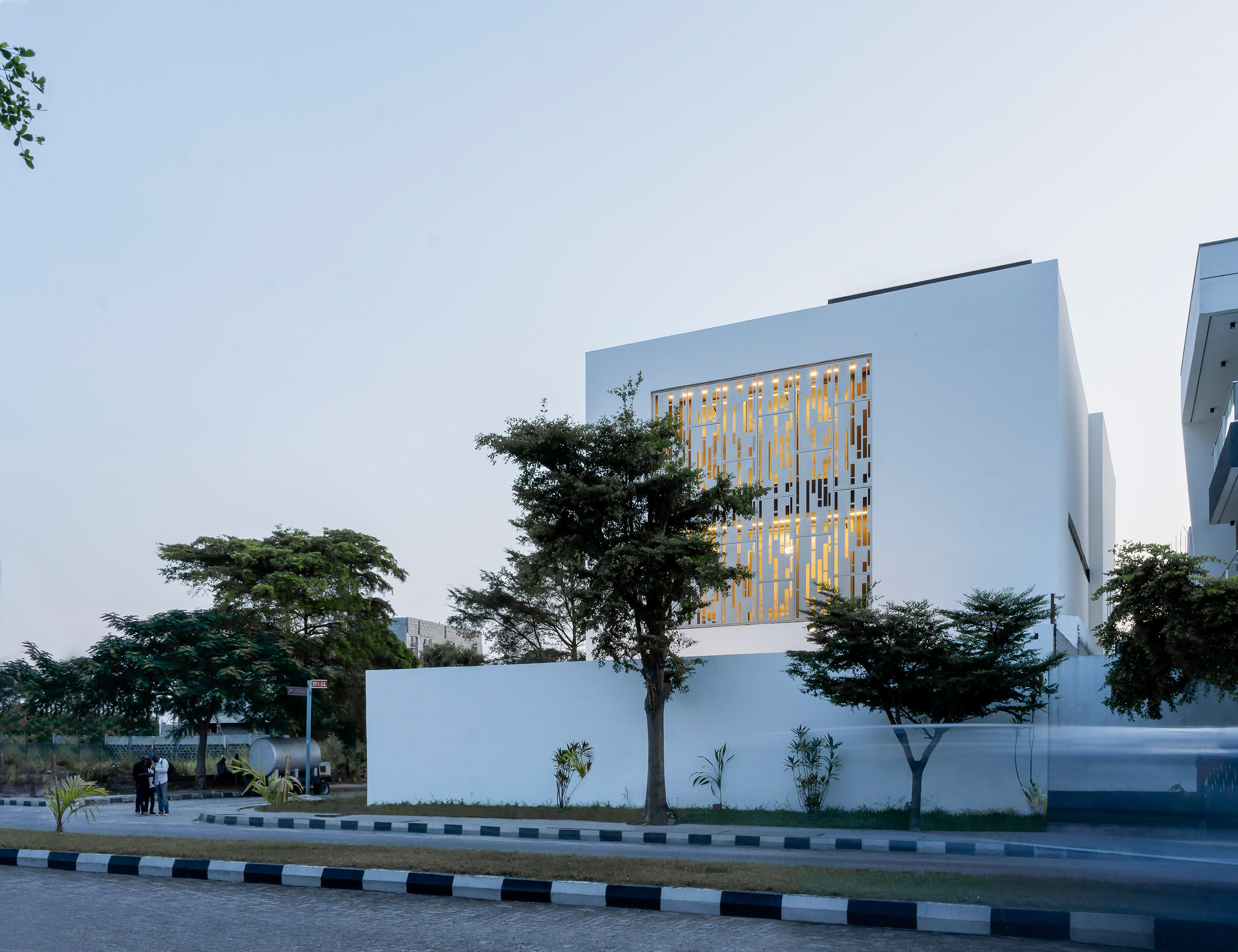 White cube house with a perforated metal opening in the facade on a street corner