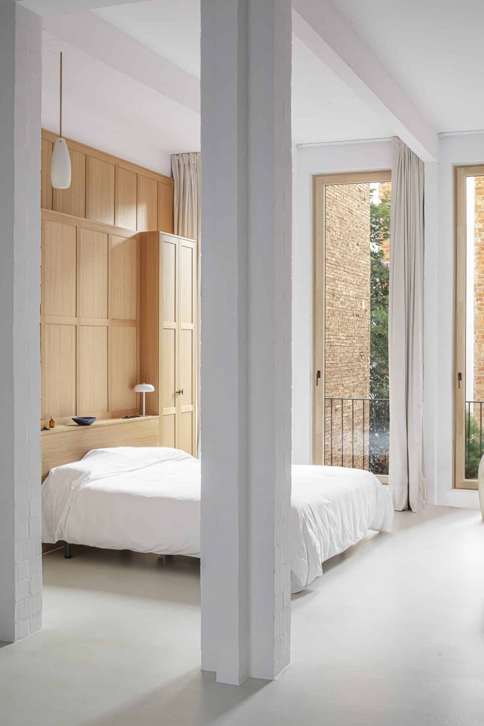 Interior of a bedroom with white floors, white square columns, wood-panelled wall and a bed with white bedding