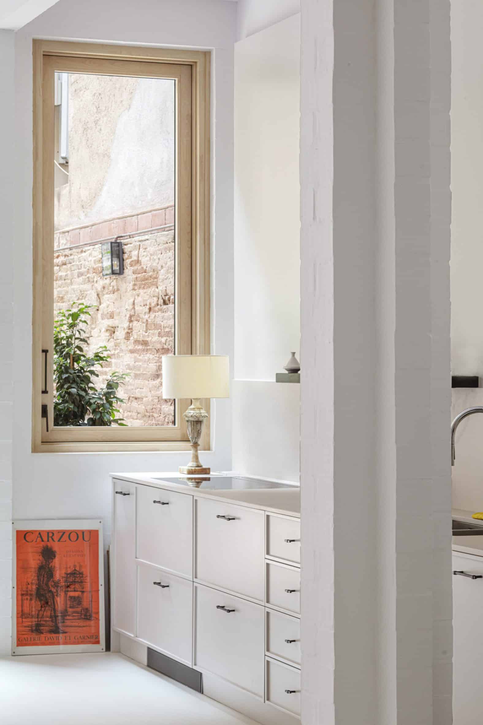 Kitchen of House 1616 with white cabinets, white floors, white walls and a wood-framed window
