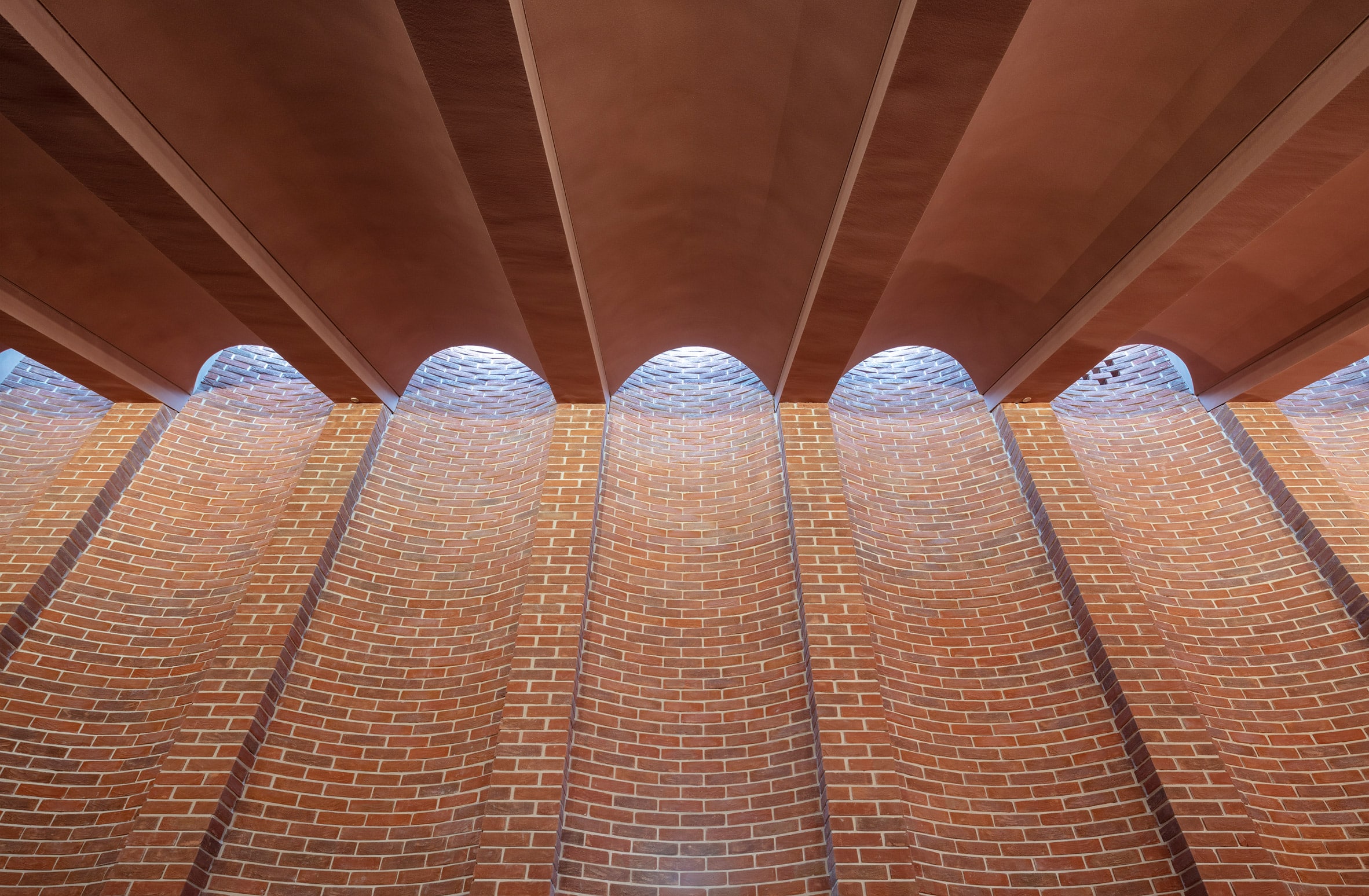 Red-brick wall with recessed bays aligning with arches in the ceiling