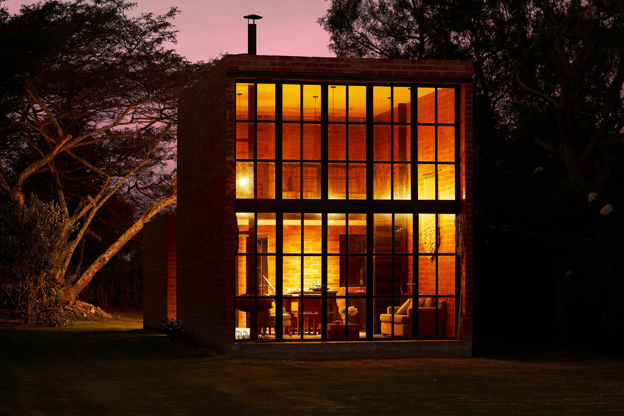Exterior of a brick micro home with double-height window facade lit up at night