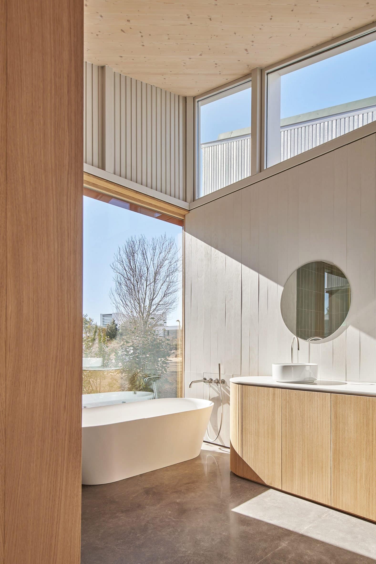 Bathroom interior with concrete walls, wooden vanity unit and white freestanding bath