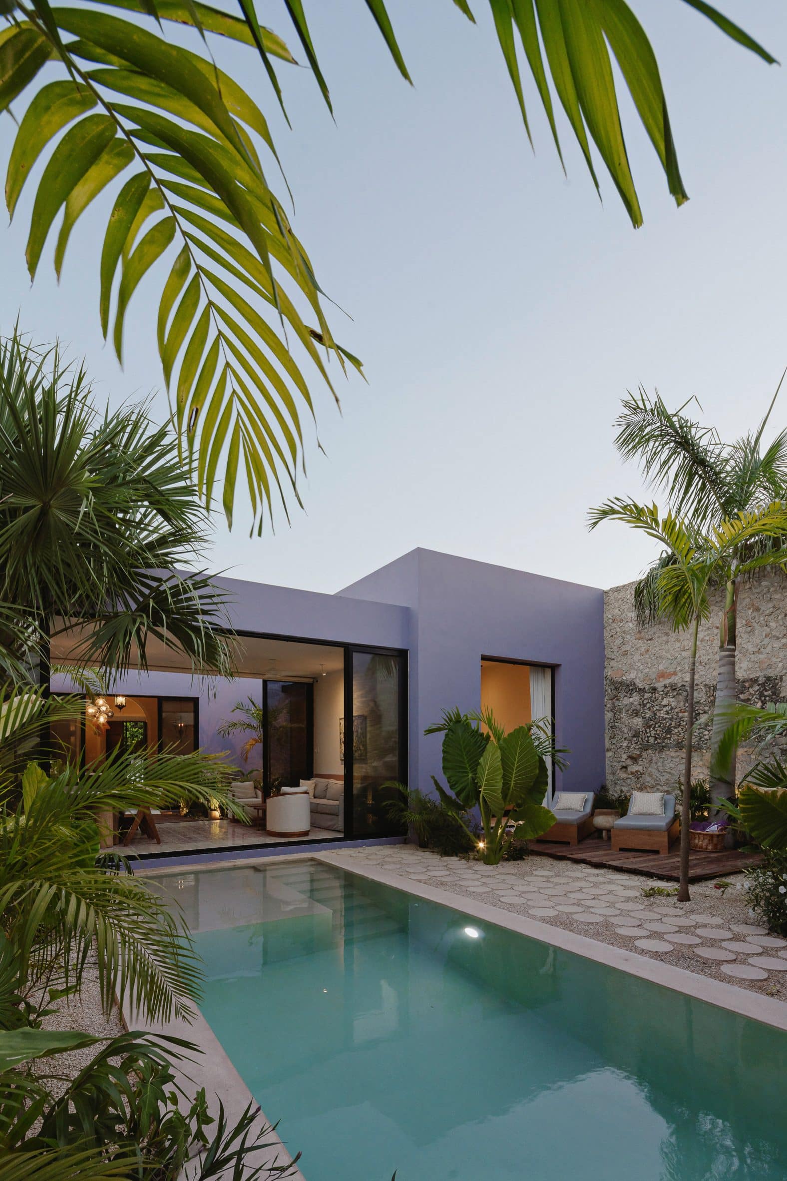Purple rectangular one-storey building with a swimming pool and palm trees