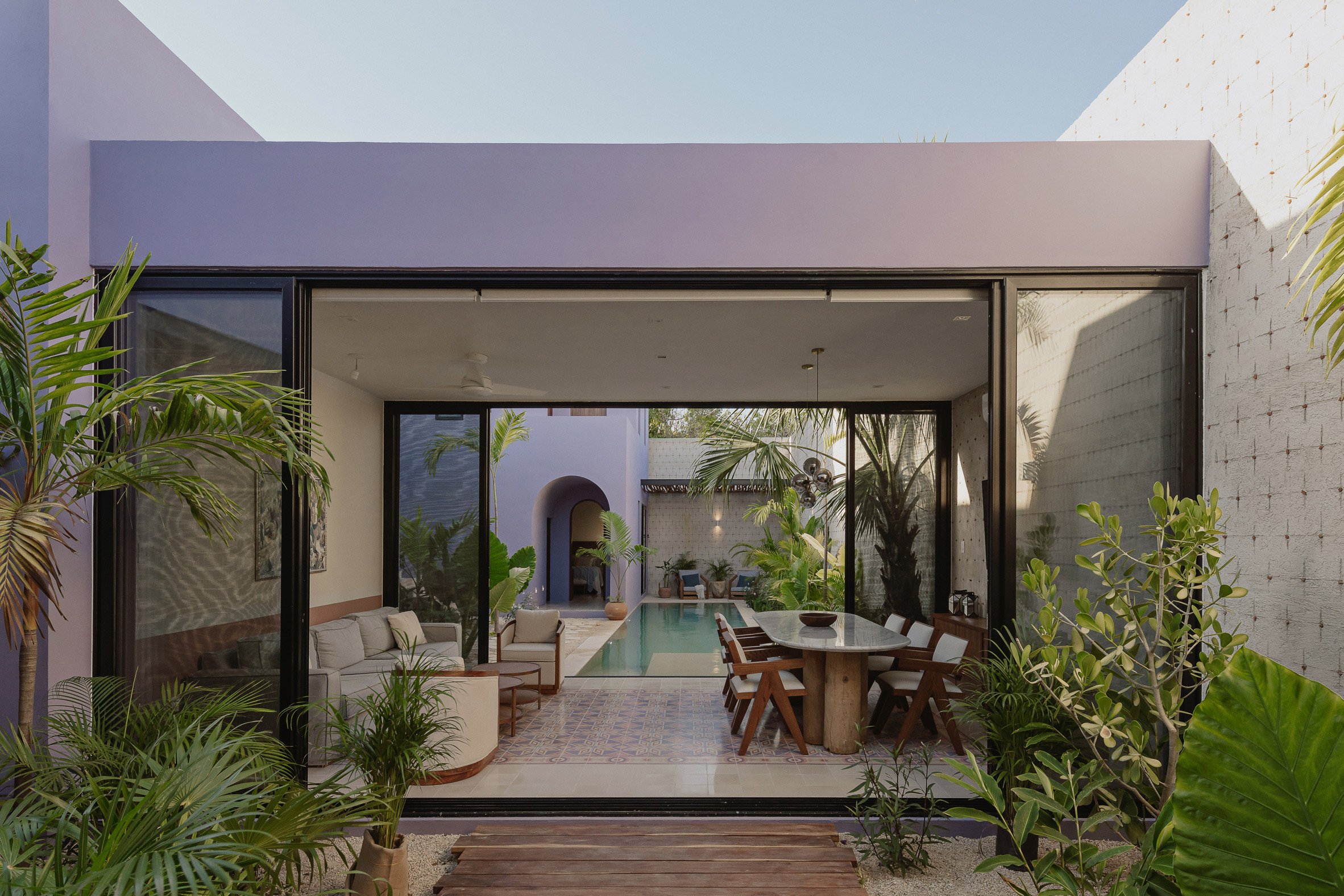 A one-storey purple building with glass sliding doors revealing a dining room and swimming pool beyond