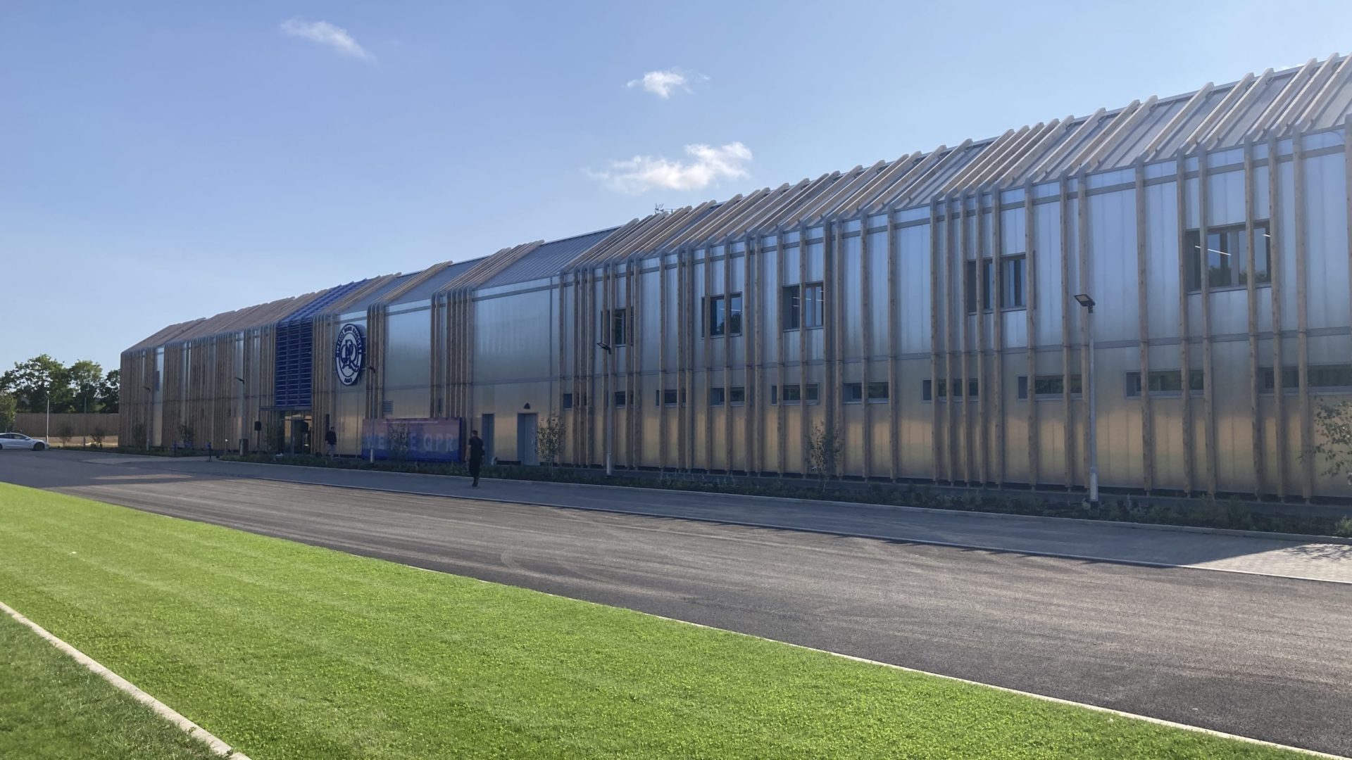 Buro Happold QPR - Outside of training ground with green turf. Blue sky with some white clouds above. 