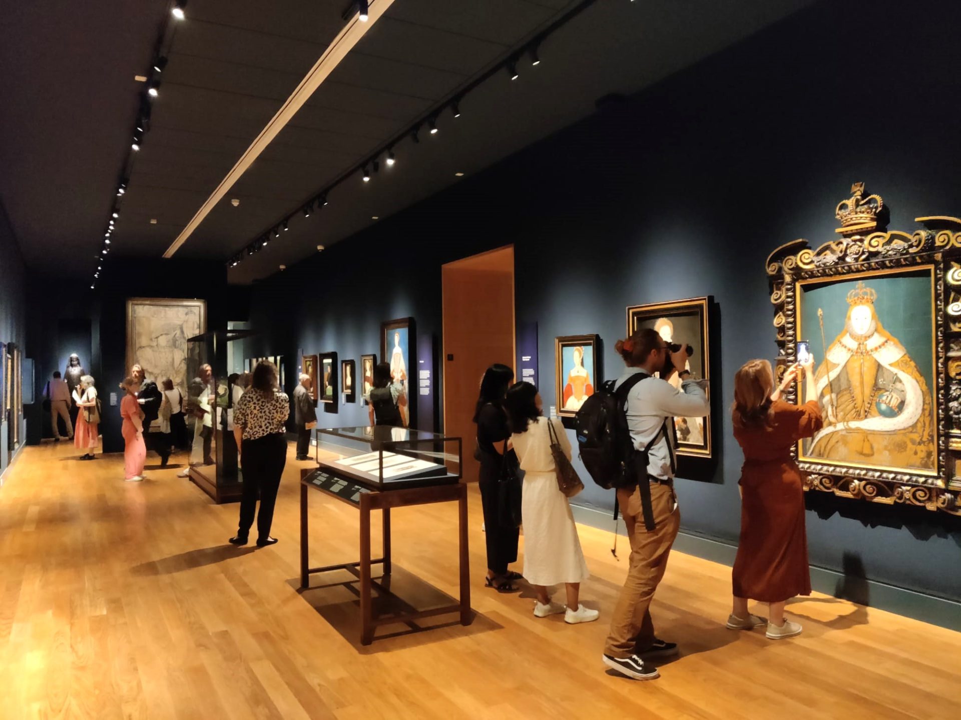 An art gallery with paintings on the blue walls and people looking at them.