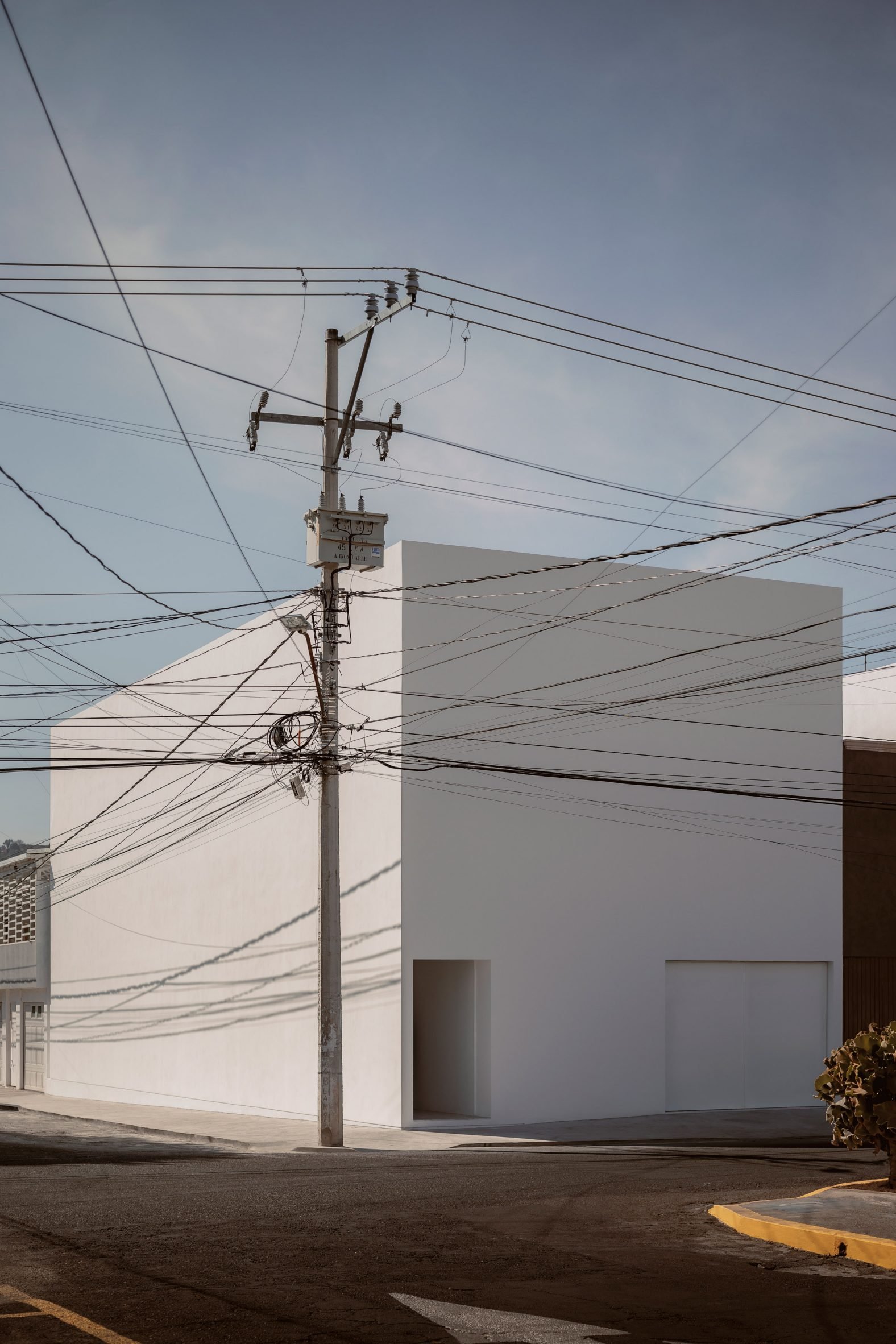 A white cube house on a street corner with telephone poles