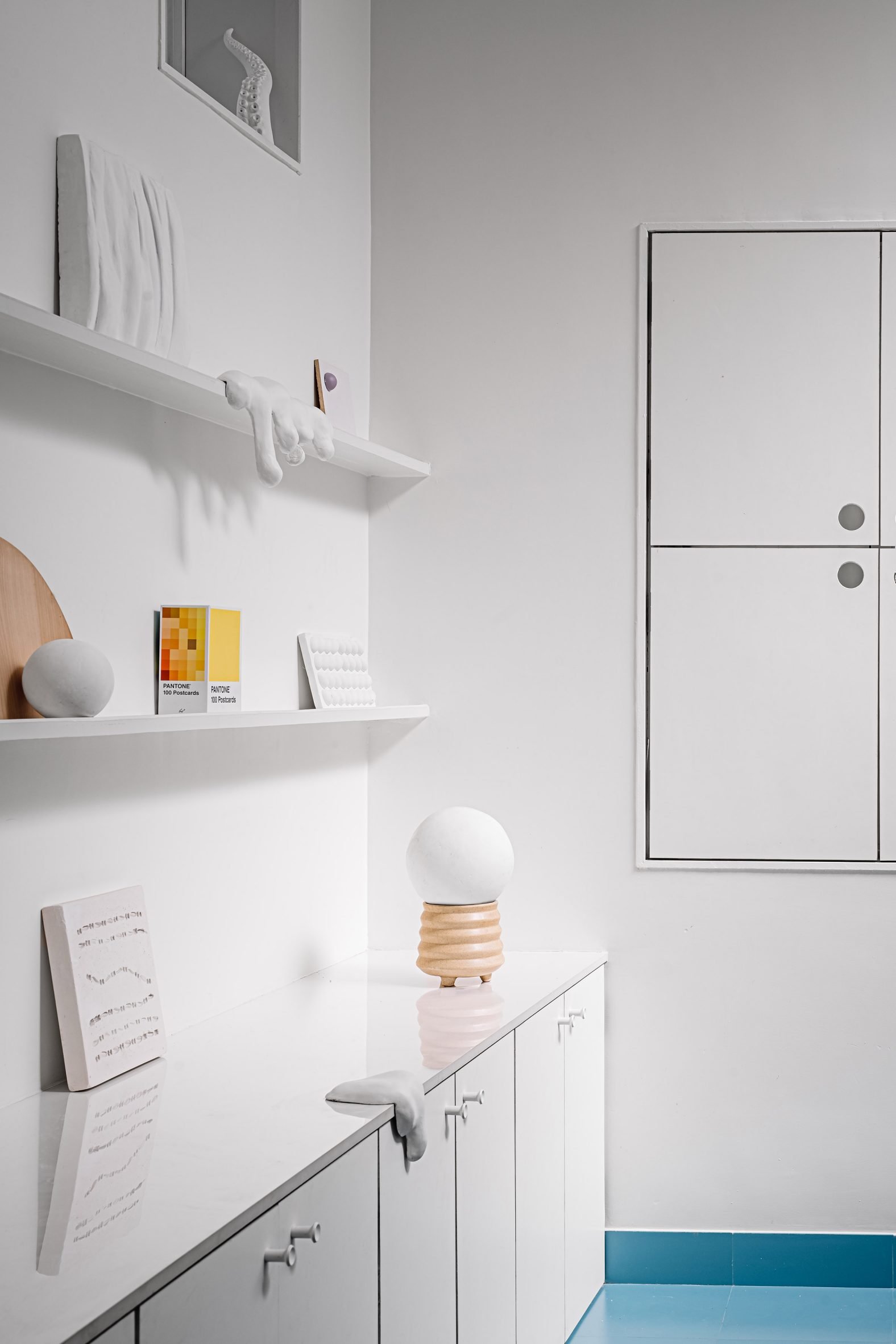 Gallery wall with objects and artworks, with cupboards in the background