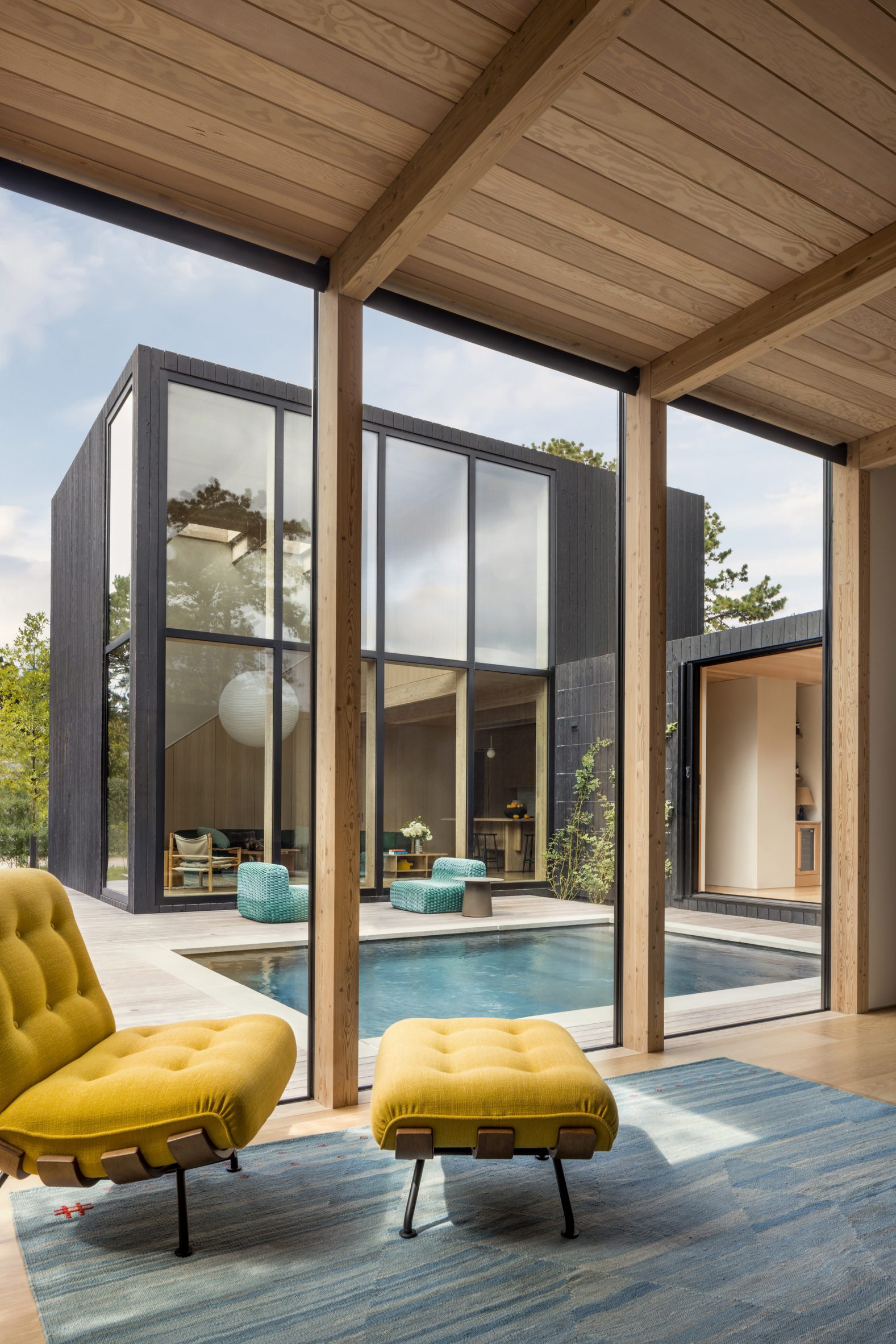 Minimalist house clad in blackened wood arranged around swimming pool