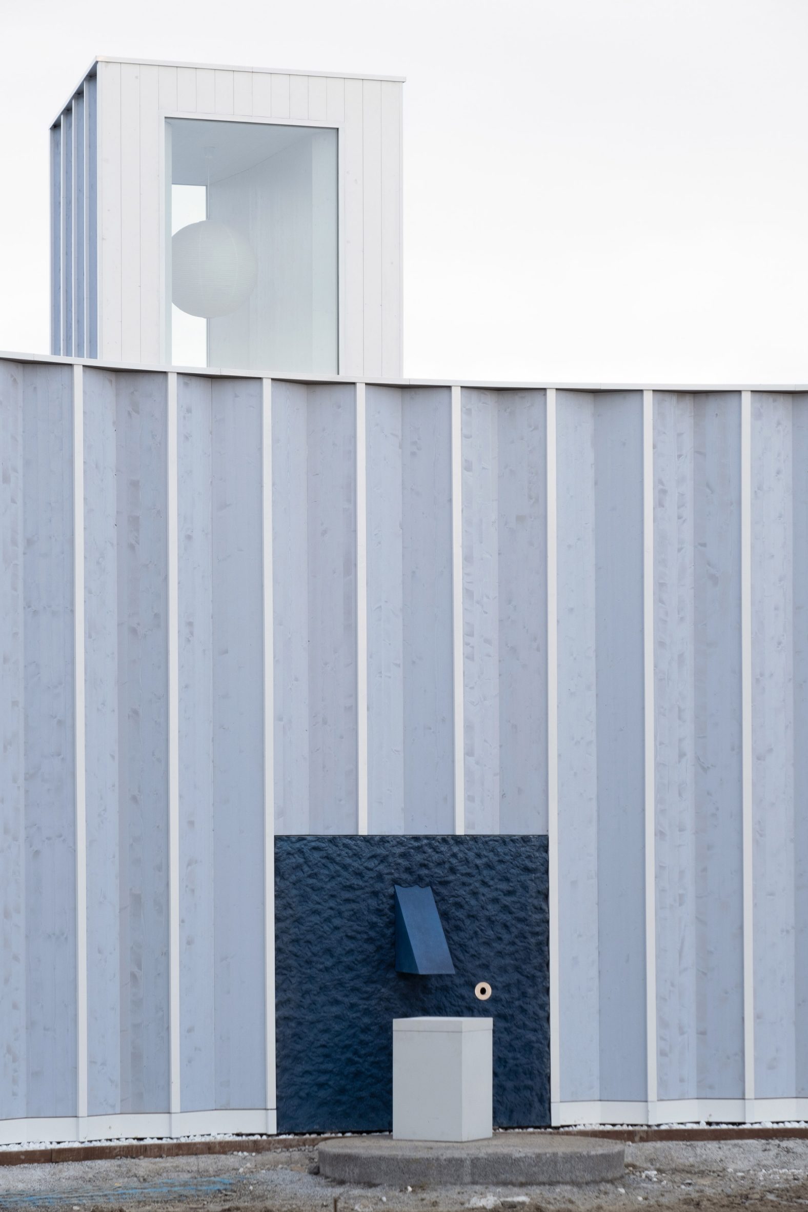 Pleated blue-timber structure with a roof lantern and blue water fountain