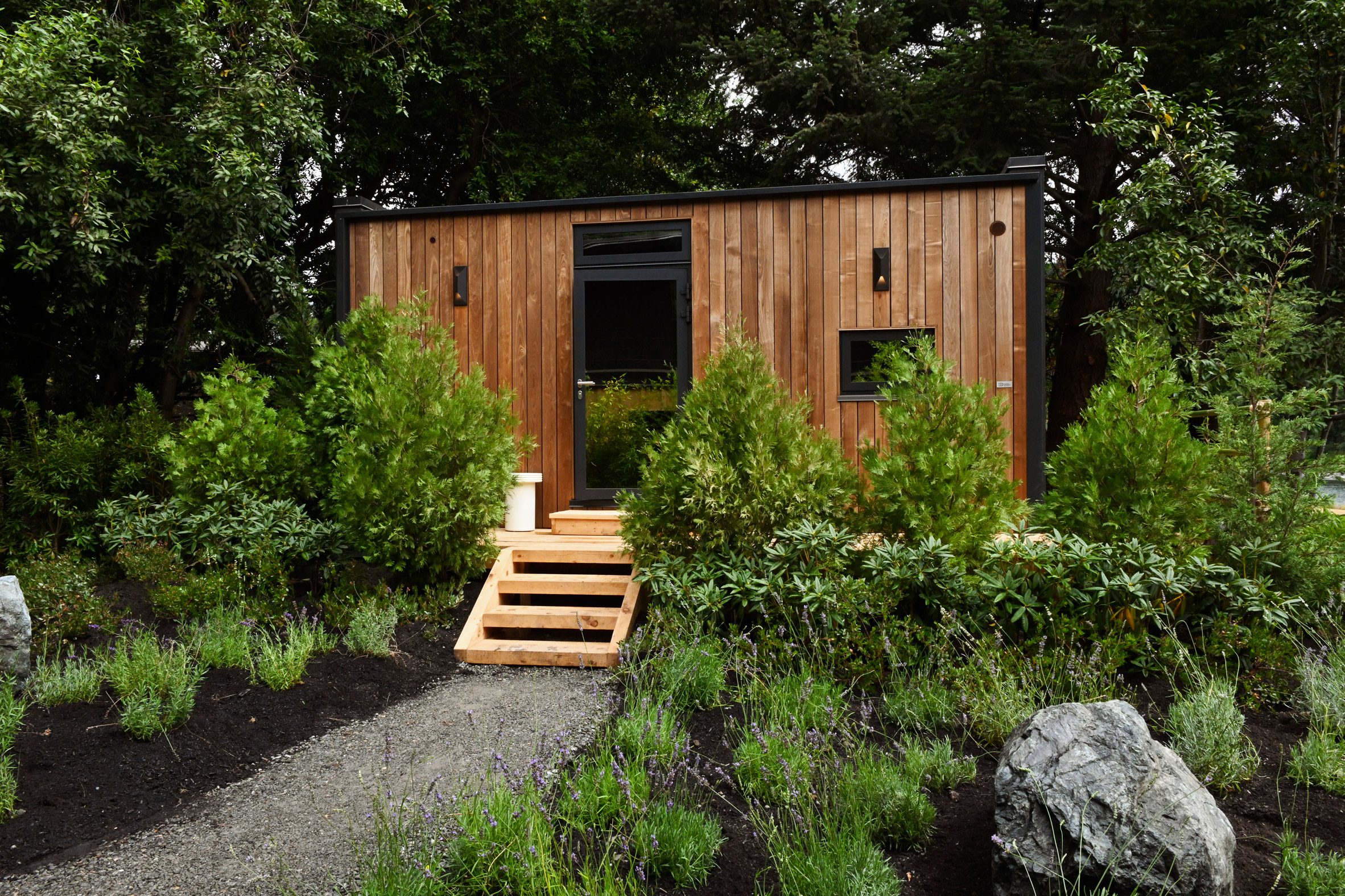 Back side of a mirrored cabin with a wooden facade and steps up to the door